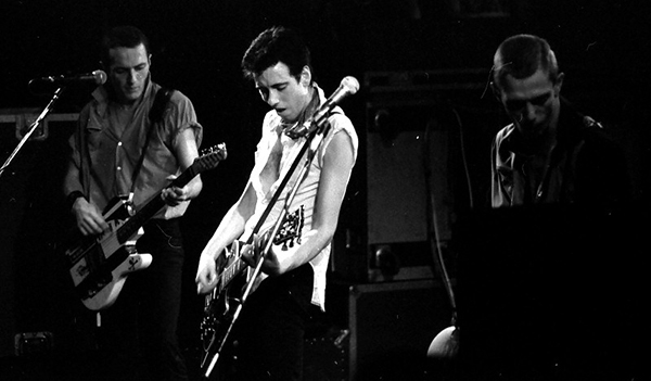 The Clash in concert, 21 May 1980. From left to right: Joe Strummer (rhythm guitar), Mick Jones (lead guitar), Paul Simonon (bass guitar). Not pictured: Topper Headon (drums). Courtesy Chateau Neuf, Oslo, Norway via Commons.wikimedia.org